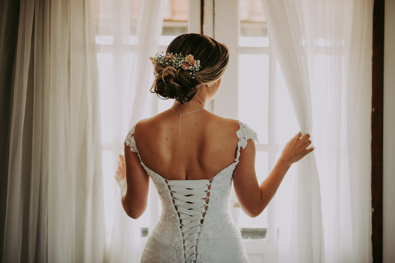 Bride from behind in a lace gown by a sunlit window